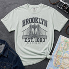 Bay colored Vintage-style Brooklyn NYC graphic t-shirt on a Bay colored Comfort Colors cotton shirt, featuring the Brooklyn Bridge and “Brooklyn Est. 1883” text.