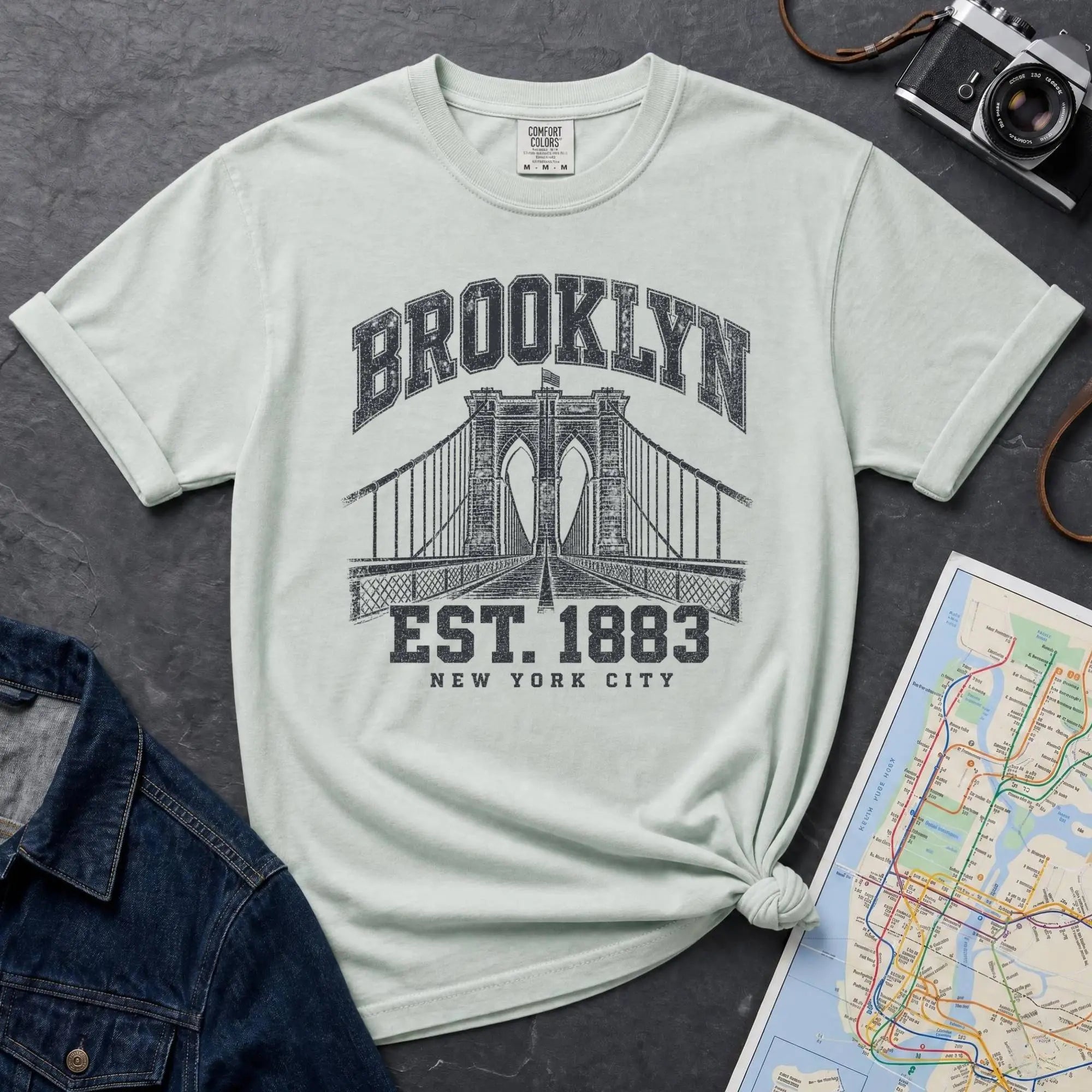 Bay colored Vintage-style Brooklyn NYC graphic t-shirt on a Bay colored Comfort Colors cotton shirt, featuring the Brooklyn Bridge and “Brooklyn Est. 1883” text.