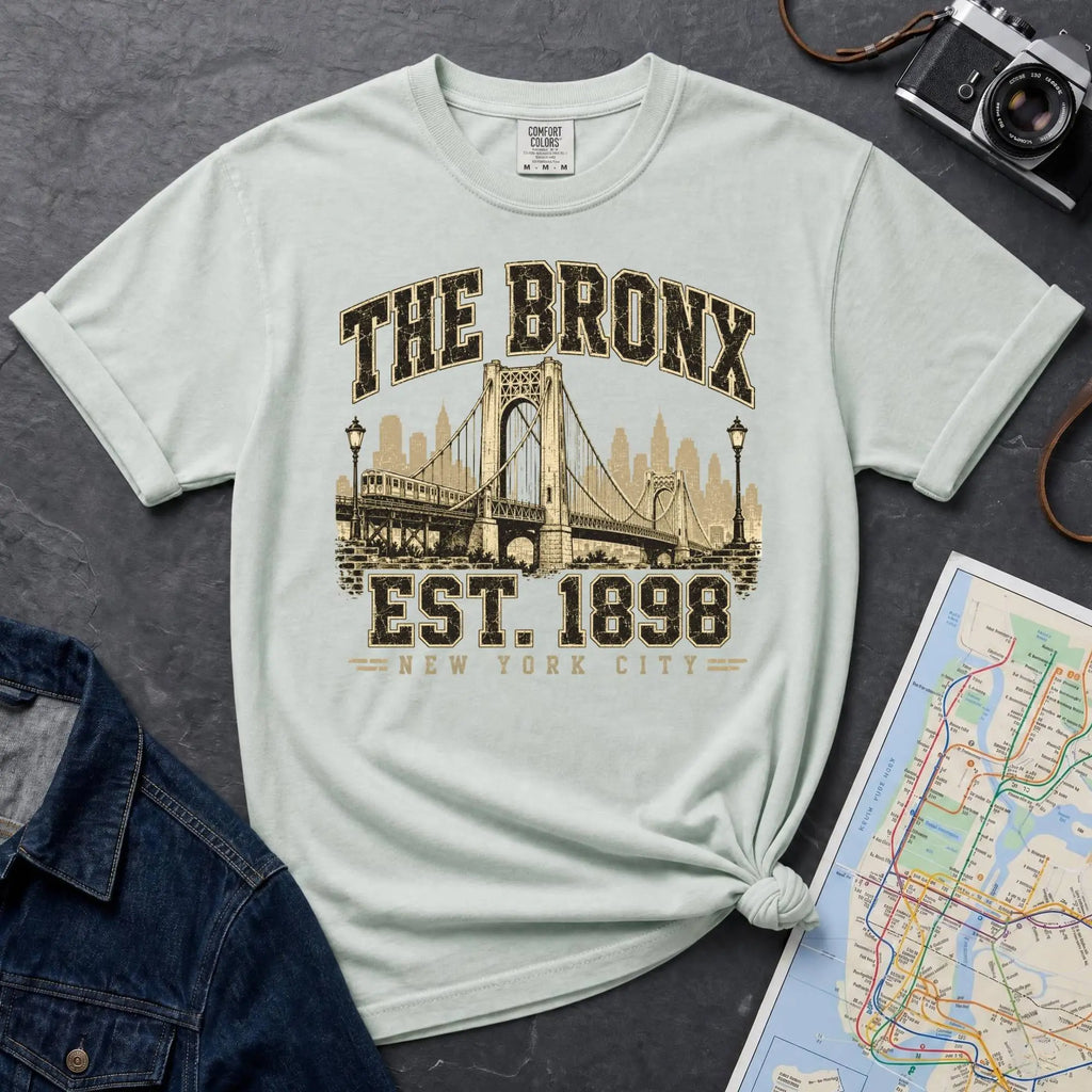 Bay colored t-shirt with 'The Bronx Est. 1898' design on a dark surface with a map and denim jacket.