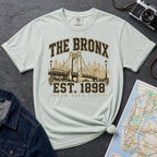 Bay colored t-shirt with 'The Bronx Est. 1898' design on a dark surface with a map and denim jacket.