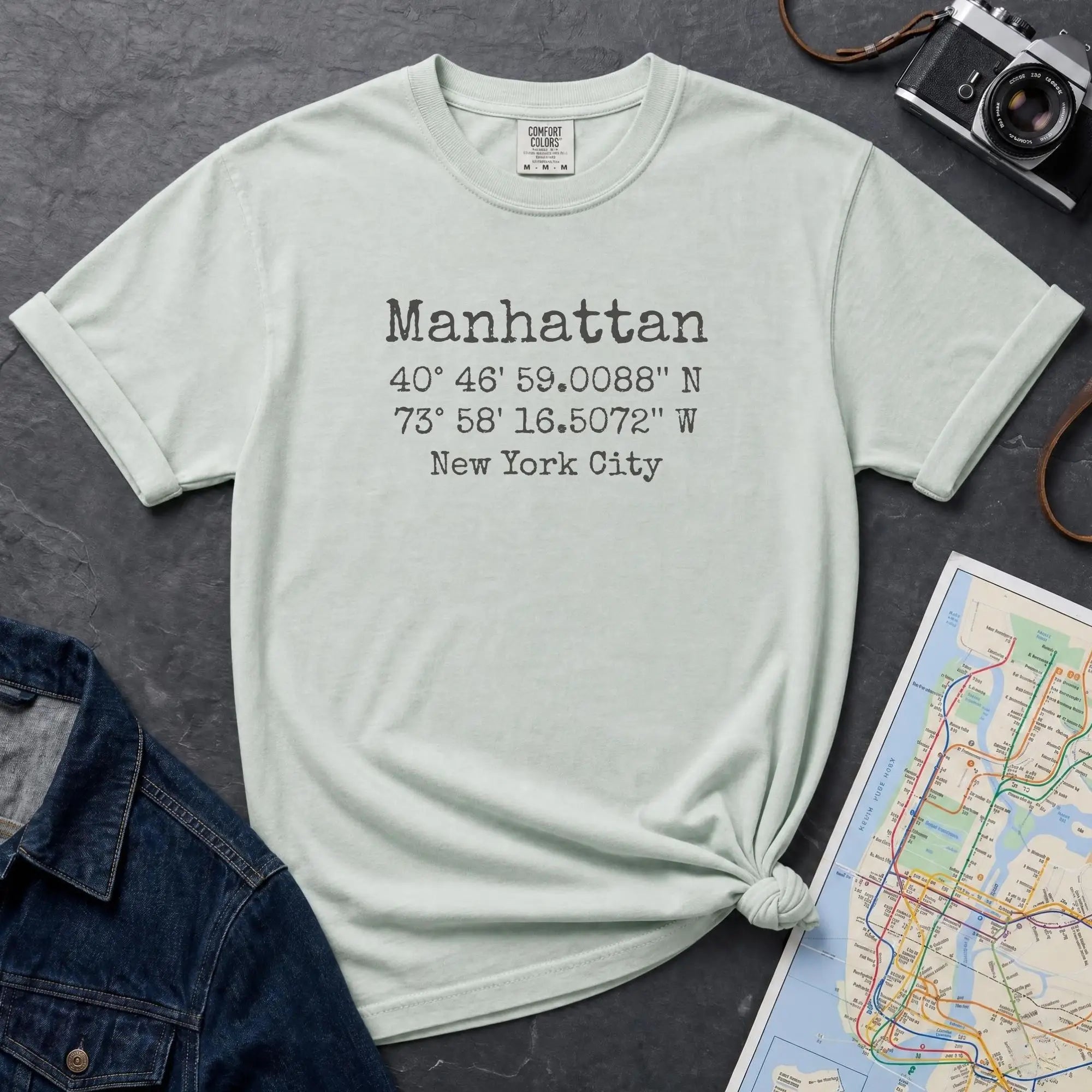 Bay colored t-shirt with Manhattan coordinates print, denim jacket, and map on a dark surface