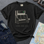 Black t-shirt with a graphic design of a train seat and text, placed on a dark surface with a map and jacket.