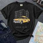 Black Comfort Colors t-shirt featuring a vintage New York City Checker Cab graphic with NYC apartment buildings and “Checker Cab • NYC • 1988” text. on a dark surface with denim jacket and map.
