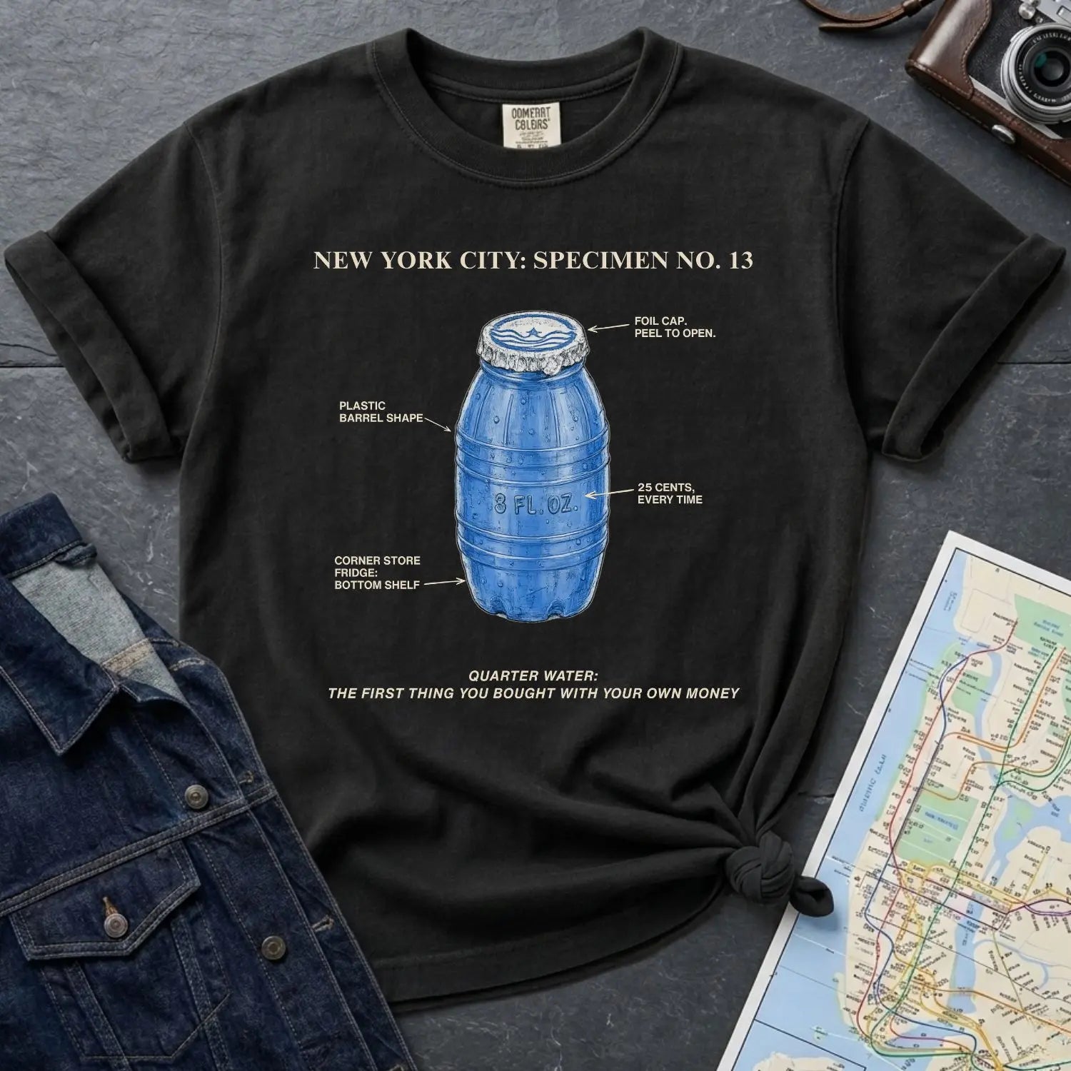 Black Comfort Colors t-shirt with blue Quarter Water graphic and text on a dark surface with denim jacket and map.