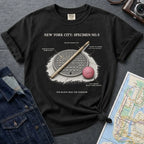 Black Comfort Colors t-shirt with a stickball graphic and text on a dark surface with denim jacket and map.