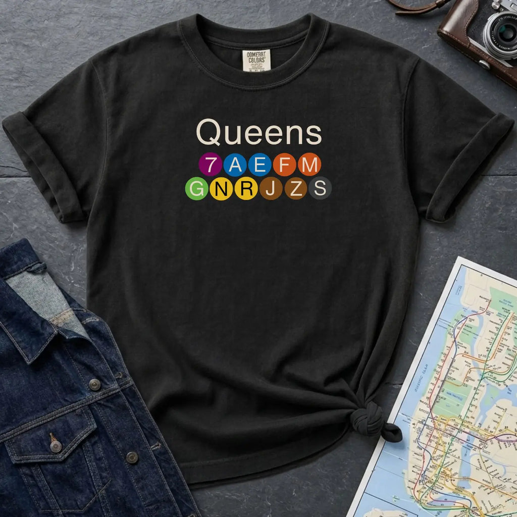 Black Comfort Colors t-shirt featuring a minimalist Queens subway line graphic with colorful NYC train icons.