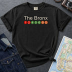Black Comfort Colors t-shirt with 'The Bronx' text and subway line design on a gray surface with a map and denim jacket.