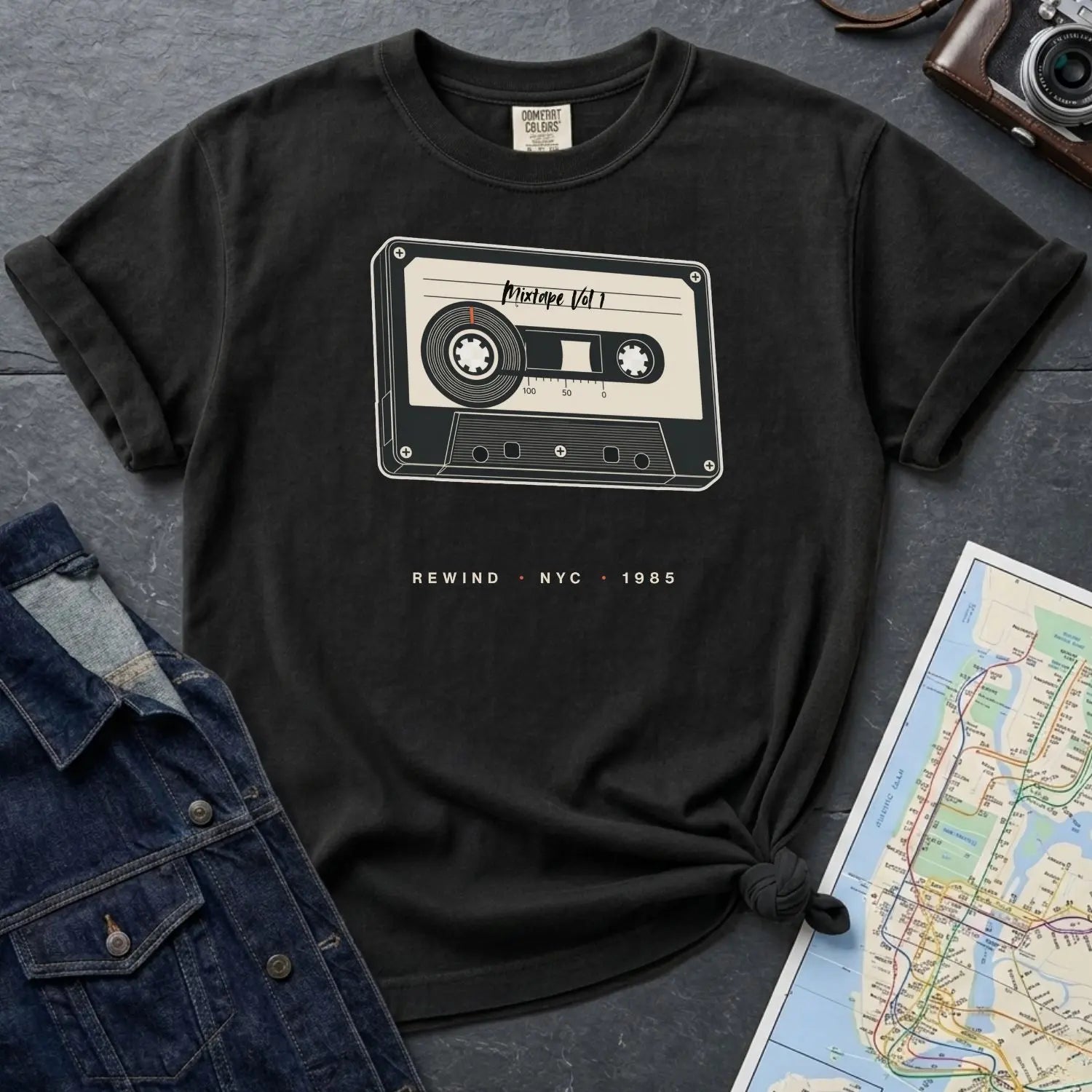 Black Comfort Colors t-shirt with a cassette tape graphic on a gray surface with denim jacket and map.