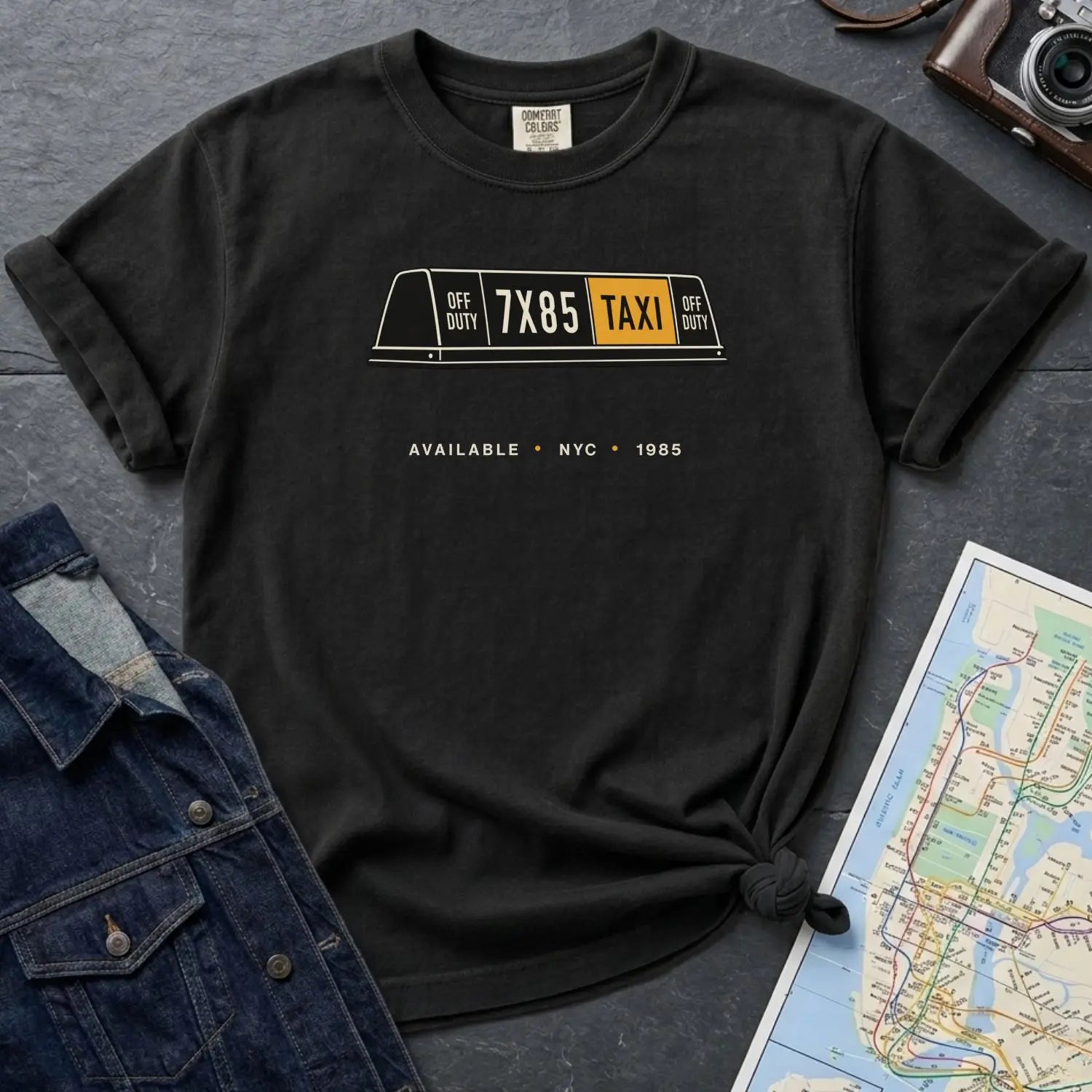 Black Comfort Colors t-shirt with NYC taxi-themed graphic on a gray surface with a denim jacket and a map.