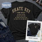 Black Comfort Colors t-shirt, back view, with Skate Key Rink Rules printed in distressed gold lettering. Rules read: No Rough Skating, One Way Traffic Only, No Trains No Chains No Tag, Last Song Is The Last Song Don't Ask. Inset shows shirt front with Skate Key Staff logo on chest.