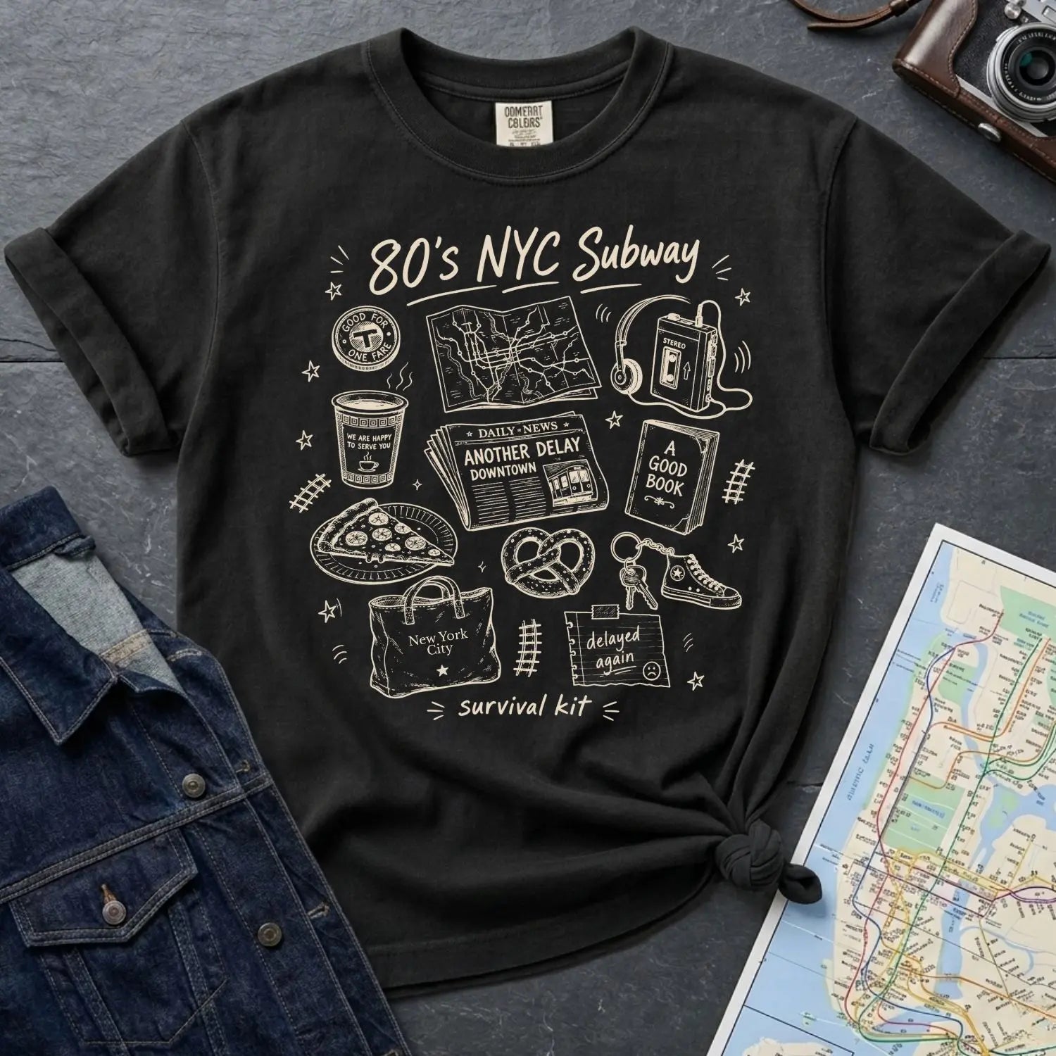 Black Comfort Colors t-shirt with '80s NYC Subway Survival Kit' graphic design on a dark surface with denim jacket and map.