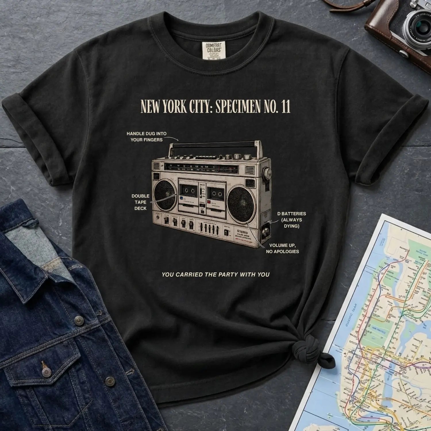 Black Comfort Colors t-shirt with a graphic of a boombox and text on a dark surface with a denim jacket and map.
