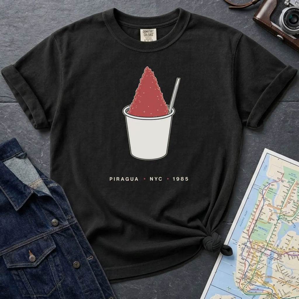 Black Comfort Colors t-shirt with a piragua graphic and text, placed on a dark surface with a map and denim jacket.
