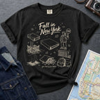 Black Comfort Colors t-shirt with 'Fall in New York' graphic design on a dark surface with a map and denim jacket.