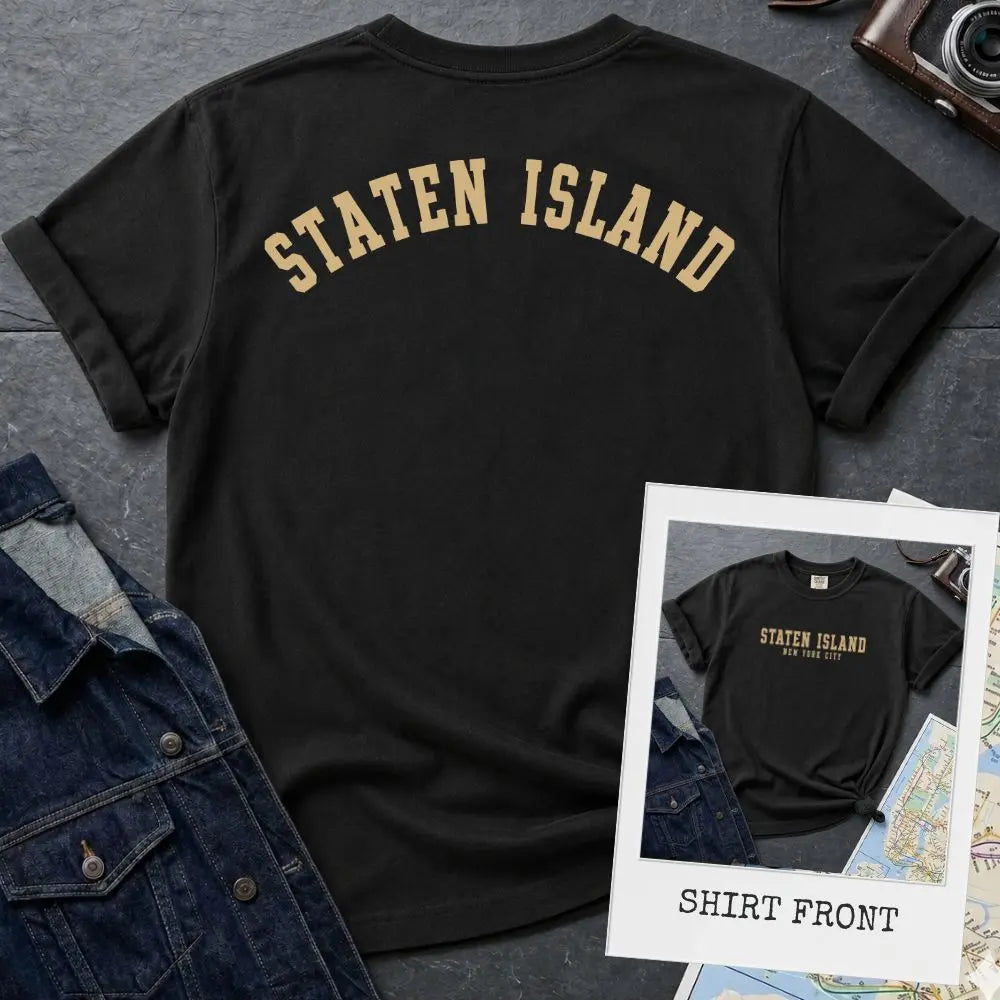 Black Comfort Colors t-shirt with 'Staten Island' text on a textured surface with a camera and denim jacket.