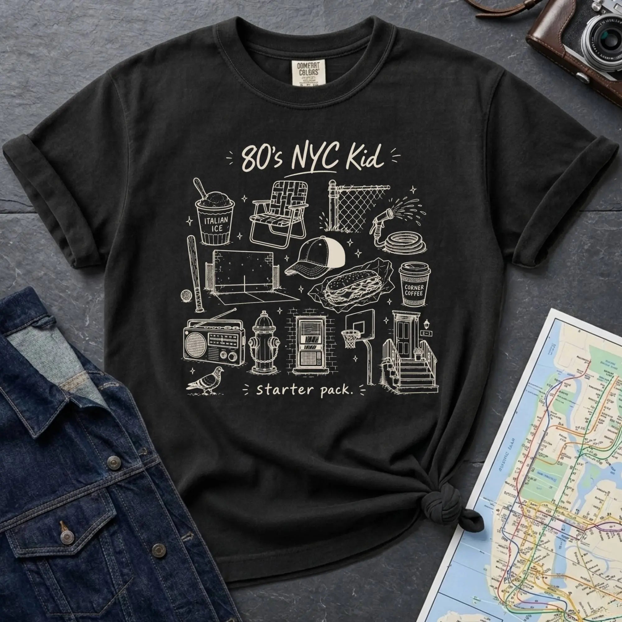 Black Comfort Colors t-shirt with an 80’s NYC Kid starter pack graphic featuring Italian ice, stickball, a fire hydrant, corner coffee, and stoop illustrations.