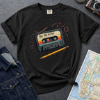 Black t-shirt with a cassette tape graphic and pencil on a gray surface with a map and denim jacket.