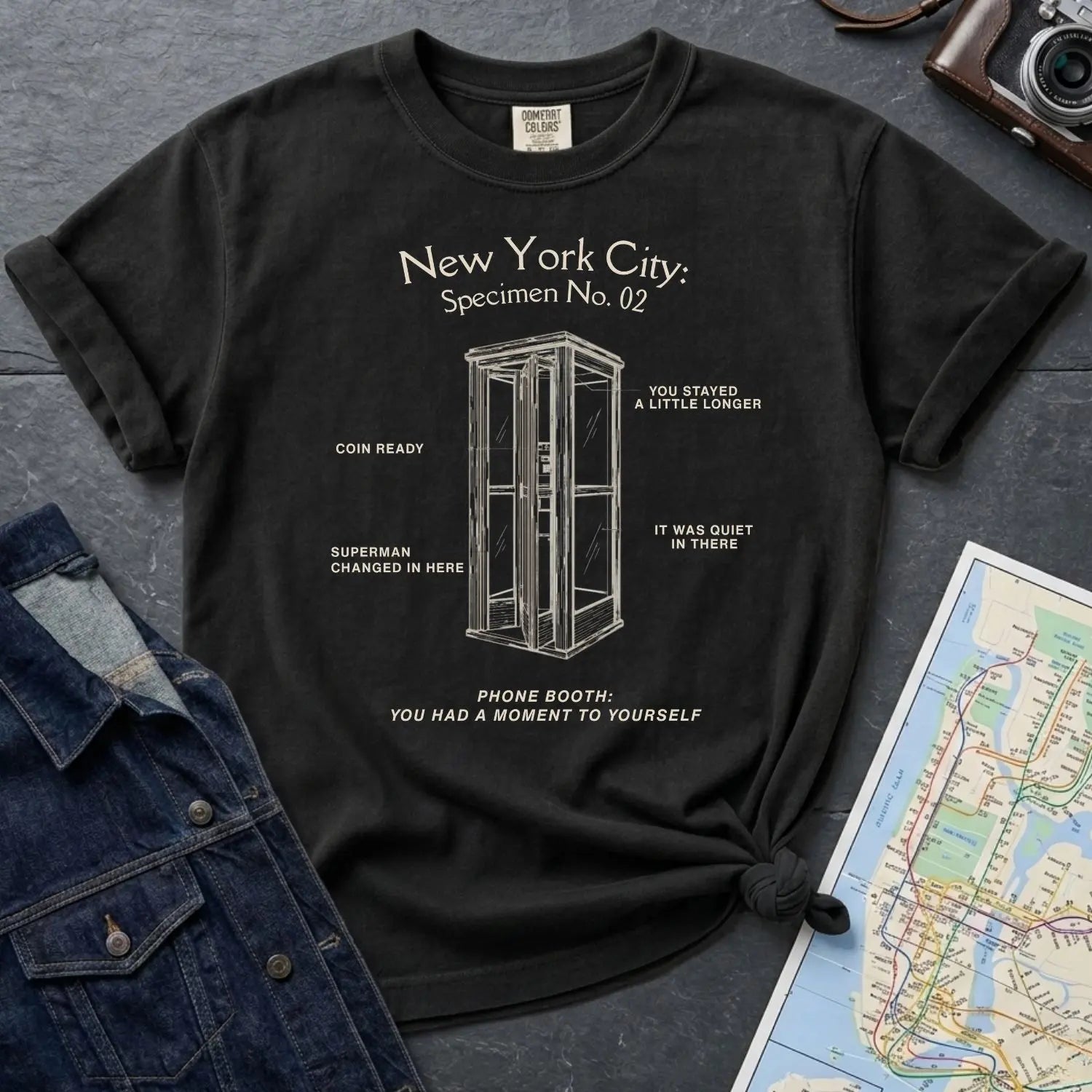 Black Comfort Colors t-shirt with phone booth design and text on a dark surface with denim jacket and map.