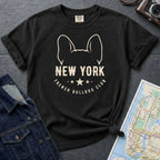 Black Comfort Colors t-shirt featuring a New York French Bulldog Club graphic with bold text, outlined French bulldog ears, stars, and a minimalist black design on a gray surface with a map and denim jacket.