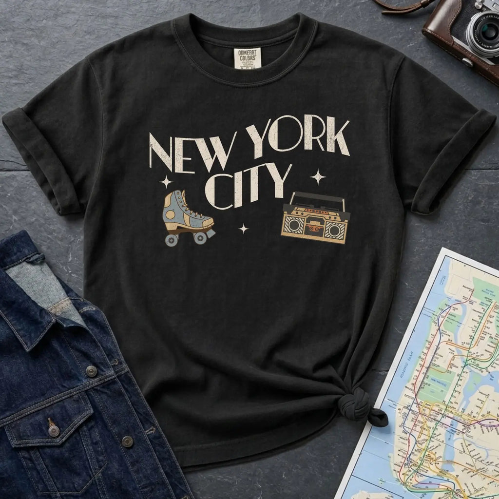 Black Comfort Colors t-shirt with 'New York City' text and a roller skate and boom box on a dark surface with a map and jacket.