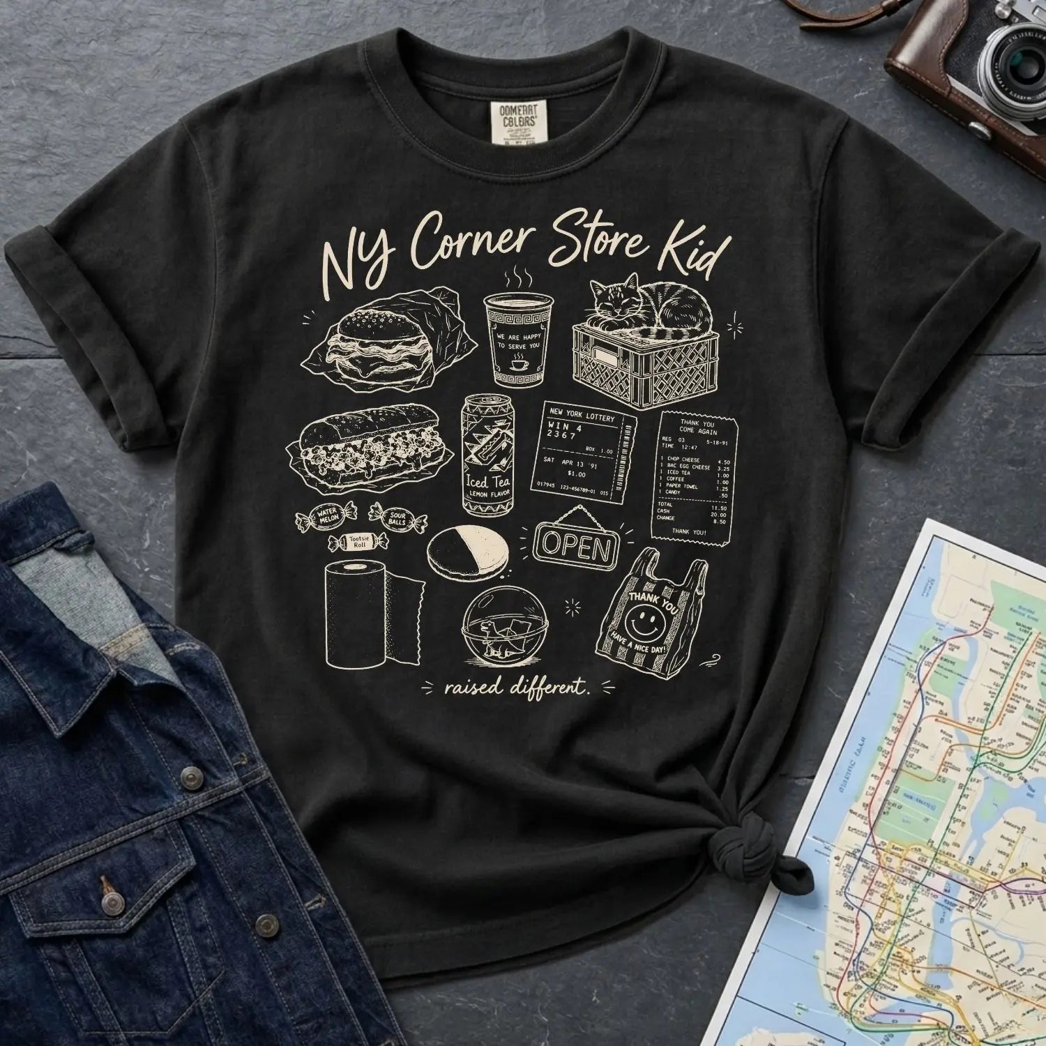 Black Comfort Colors t-shirt with 'NY Corner Store Kid' text and images on a gray surface with denim jacket and map