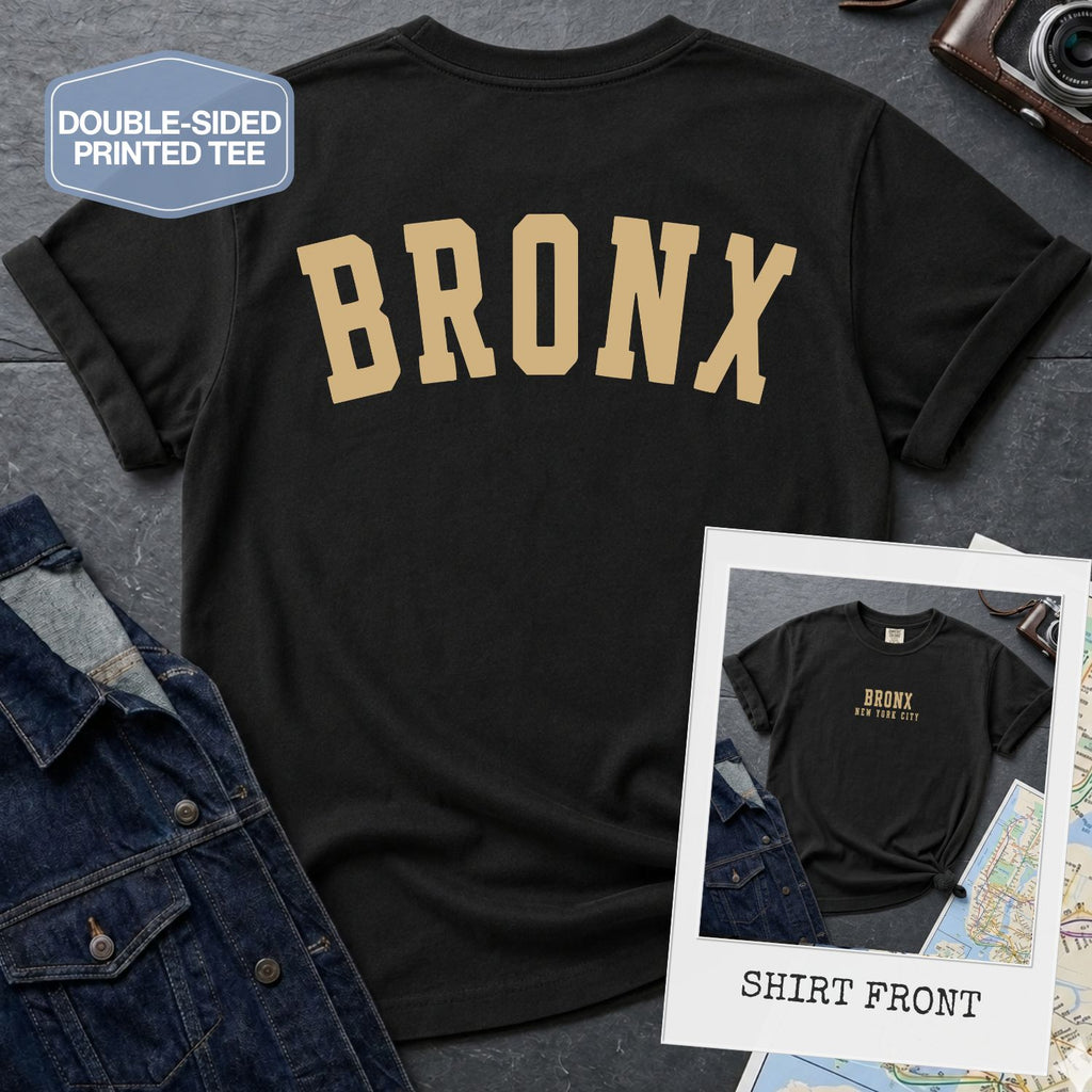 Black Comfort Colors t-shirt with 'BRONX' printed on the back of it, displayed on a gray surface.