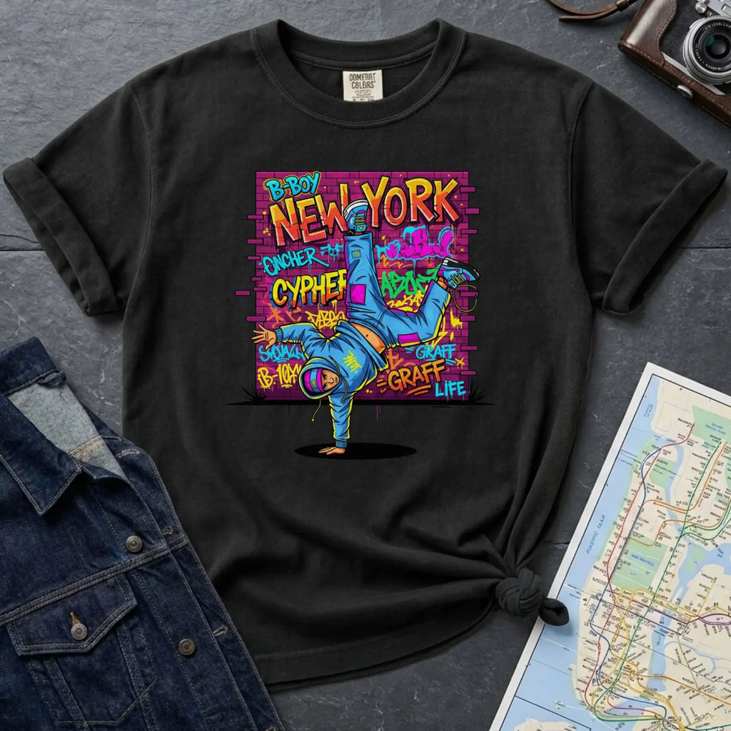 Black Comfort Colors t-shirt with a colorful graphic design featuring a breakdancer and text on a dark surface with a denim jacket and a map.