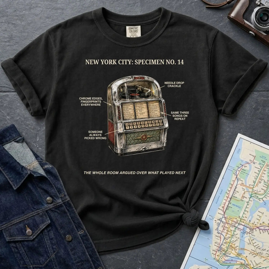Black Comfort Colors t-shirt with a vintage jukebox graphic and text on a dark surface with a denim jacket and a map.