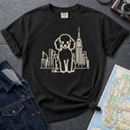 Black Comfort Colors t-shirt with a Poodle and cityscape design on a gray surface with a map and jacket.