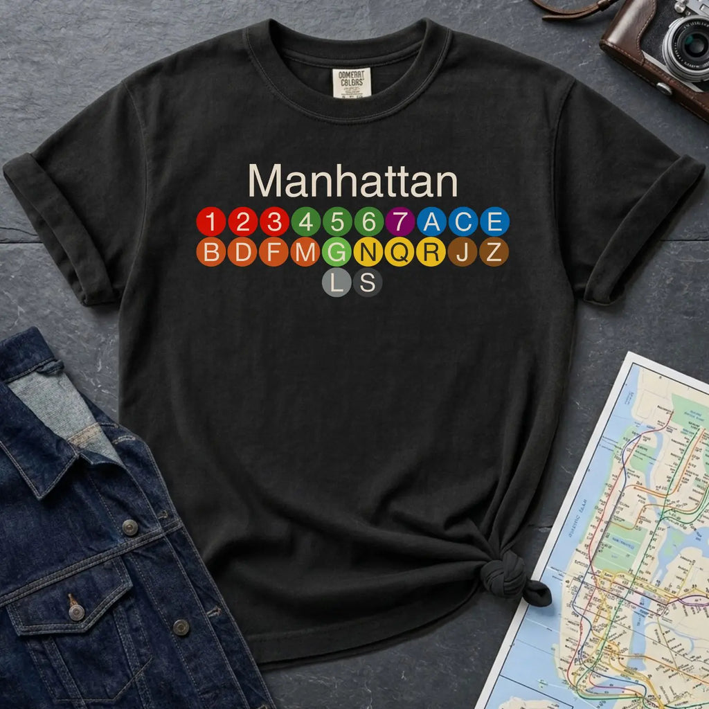 Black Comfort Colors t-shirt with Manhattan text and subway line design on a gray surface with a map and jacket.