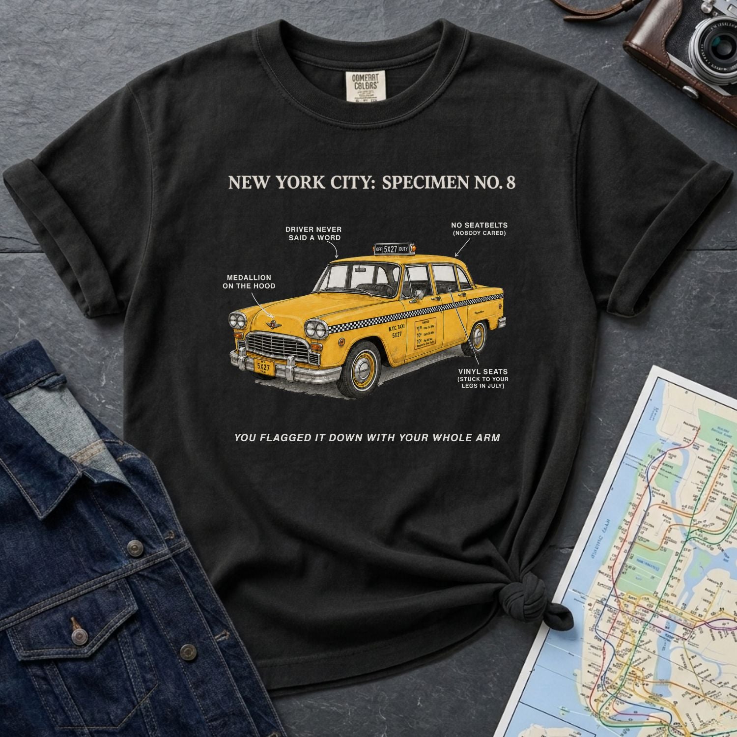 Black Comfort Colors t-shirt with yellow taxi graphic and text on a dark surface with denim jacket and map.