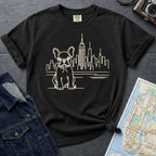 Black Comfort Colors t-shirt with a French Bulldog and cityscape design on a gray surface with a map and denim jacket.