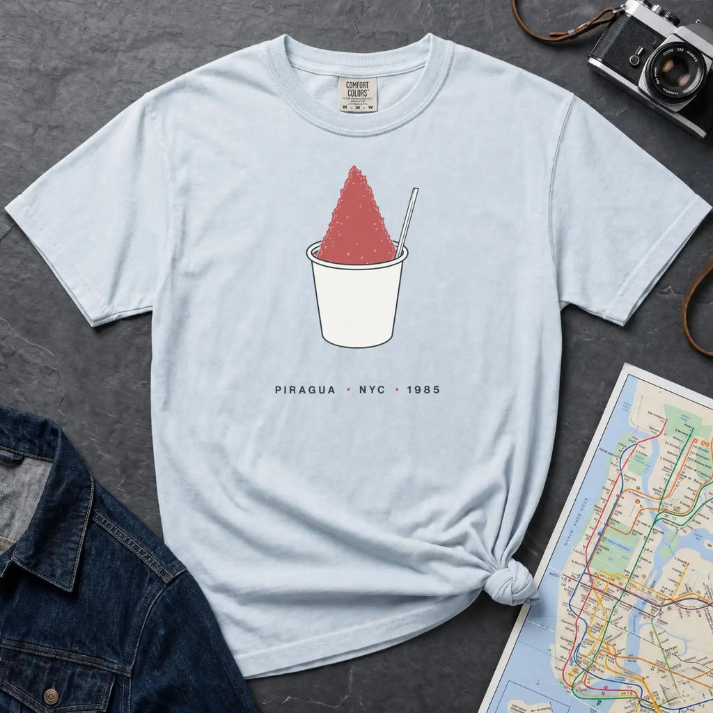 Light blue Comfort Colors t-shirt with a piragua graphic and text, placed on a dark surface with a map and denim jacket.