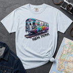 Light blue t-shirt with a colorful train graphic and 'New York' text on a gray surface with a map and denim jacket.