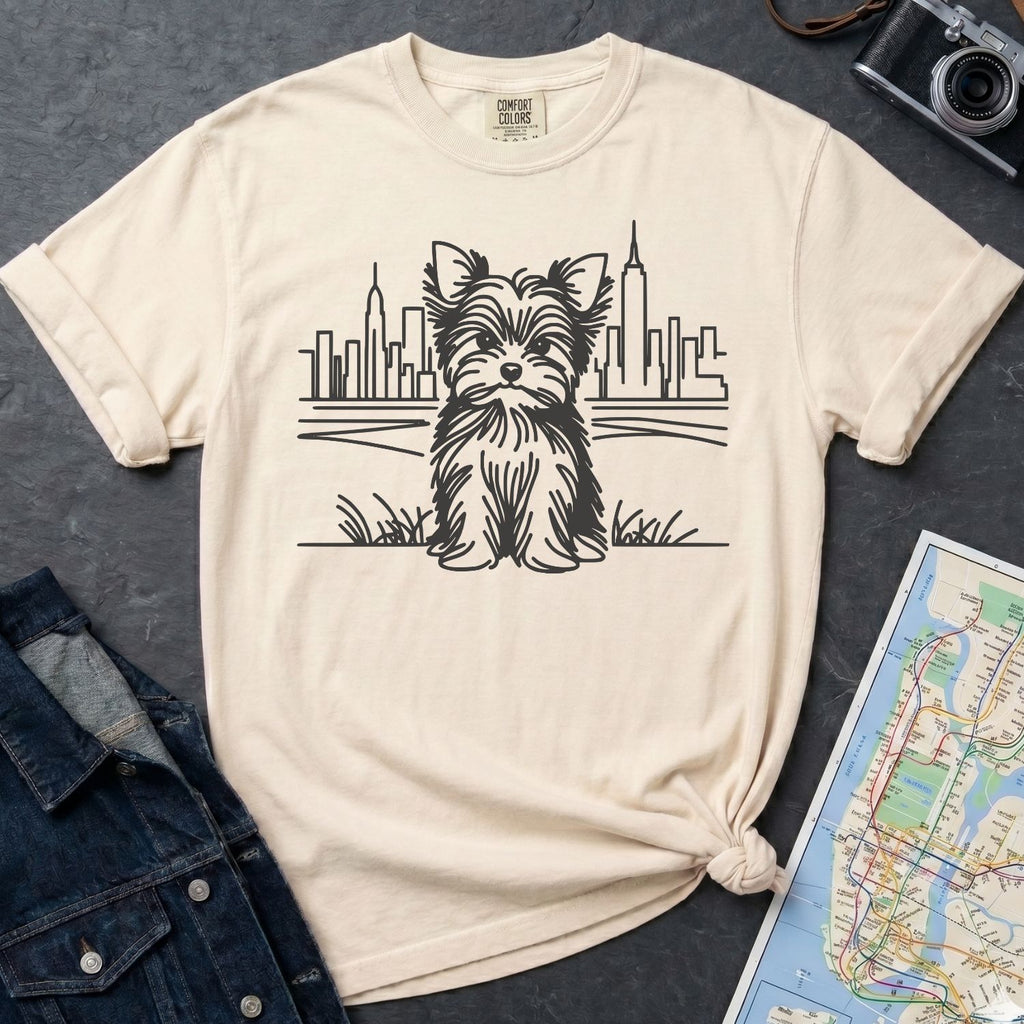 Ivory Comfort Colors t-shirt featuring a minimalist Yorkshire Terrier (Yorkie) illustration in front of the New York City skyline on a dark surface with a denim jacket and a map.