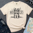 Ivory Comfort Colors t-shirt featuring a minimalist Yorkshire Terrier (Yorkie) illustration in front of the New York City skyline on a dark surface with a denim jacket and a map.