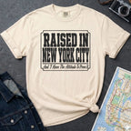 Ivory t-shirt with 'Raised in New York City' text on a dark surface with a jean jacket and a map.