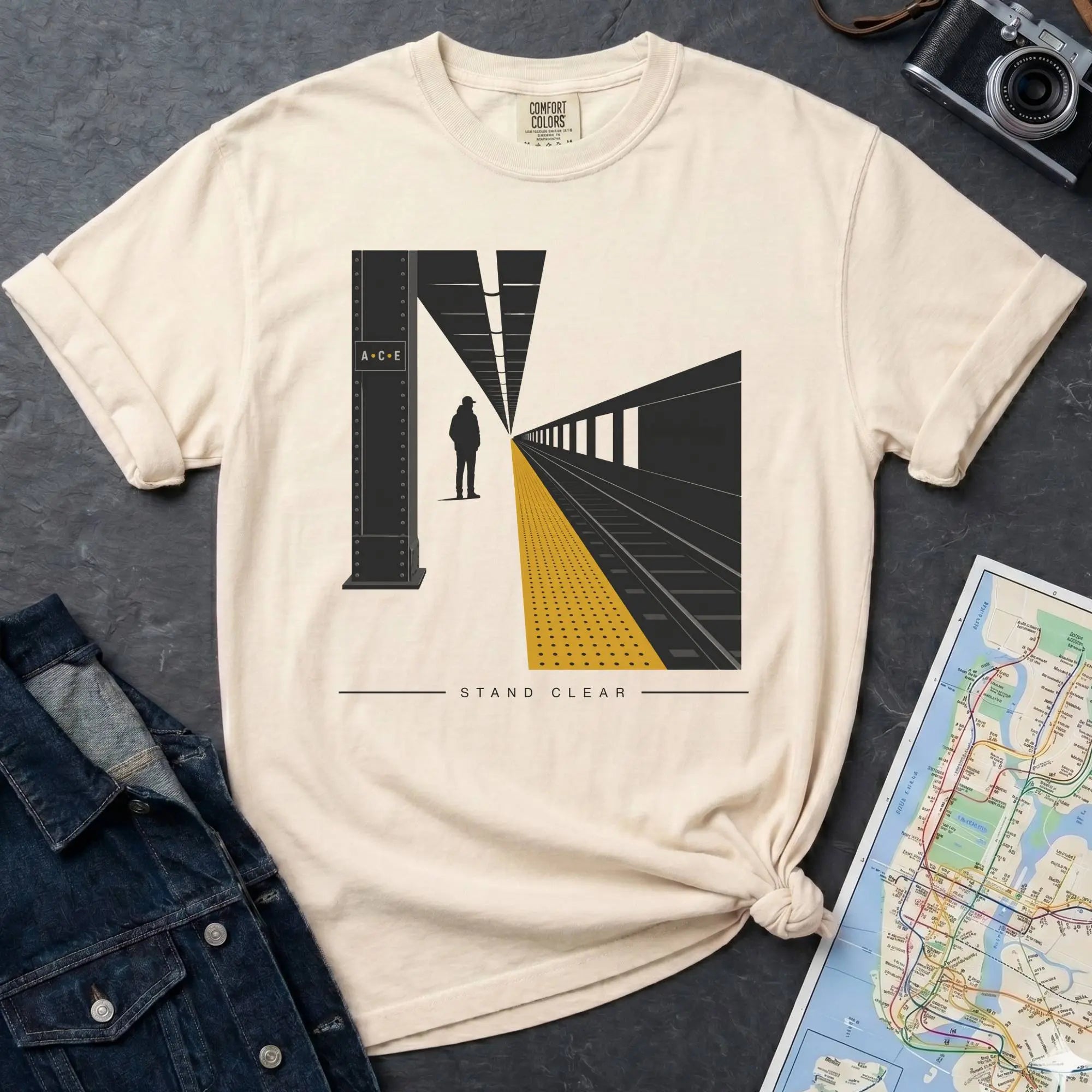Beige t-shirt with a graphic design of a train station platform, denim jacket, and map on a dark surface
