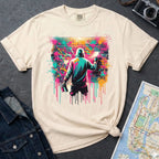 Ivory t-shirt with a graphic of a person spray painting a colorful mural on a brick wall.