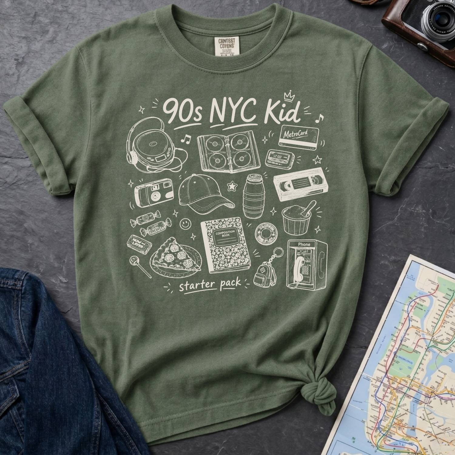 Moss t-shirt with '90s NYC Kid' graphic design on a dark surface with a denim jacket and a map.