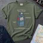 Moss green t-shirt with a newspaper box graphic and text on a textured surface with a camera and map.