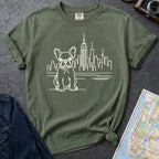 Moss green t-shirt with a French Bulldog and cityscape design on a gray surface with a denim jacket and a map.