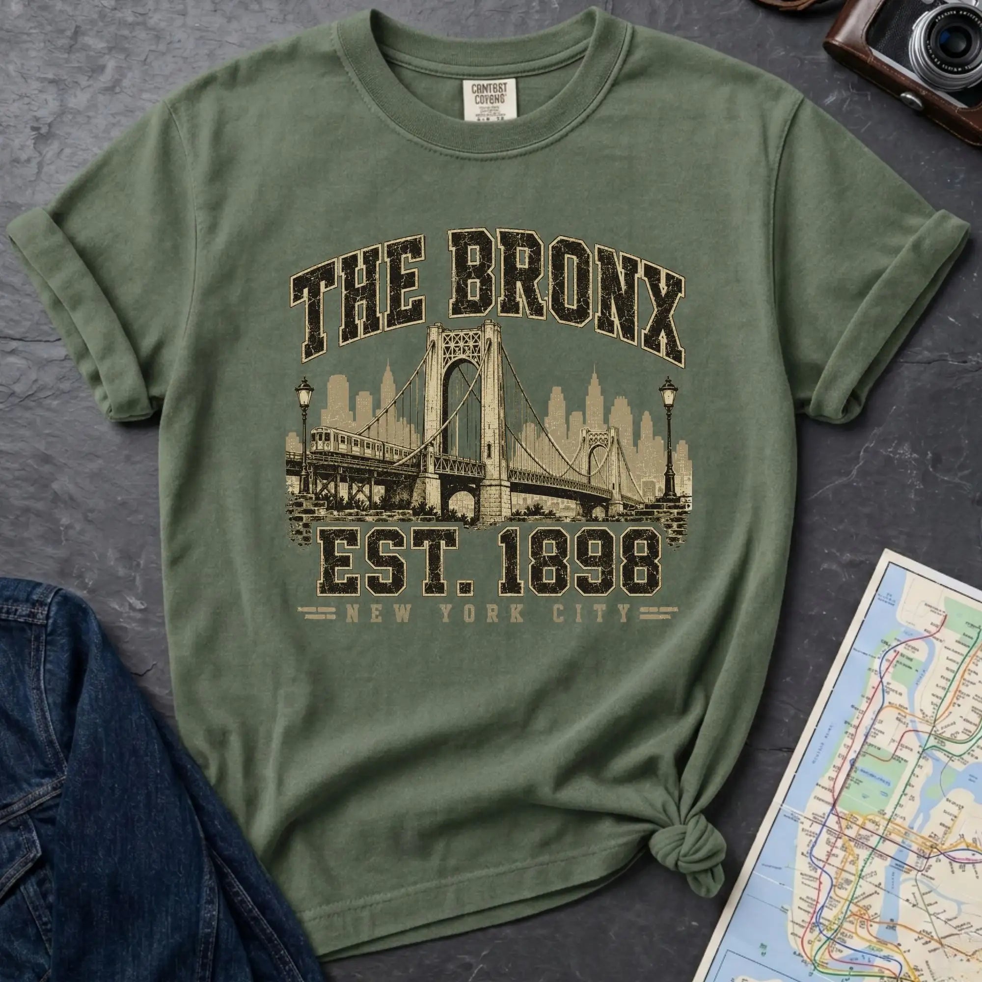 Green t-shirt with 'The Bronx Est. 1898' design on a dark surface with a map and jeans.