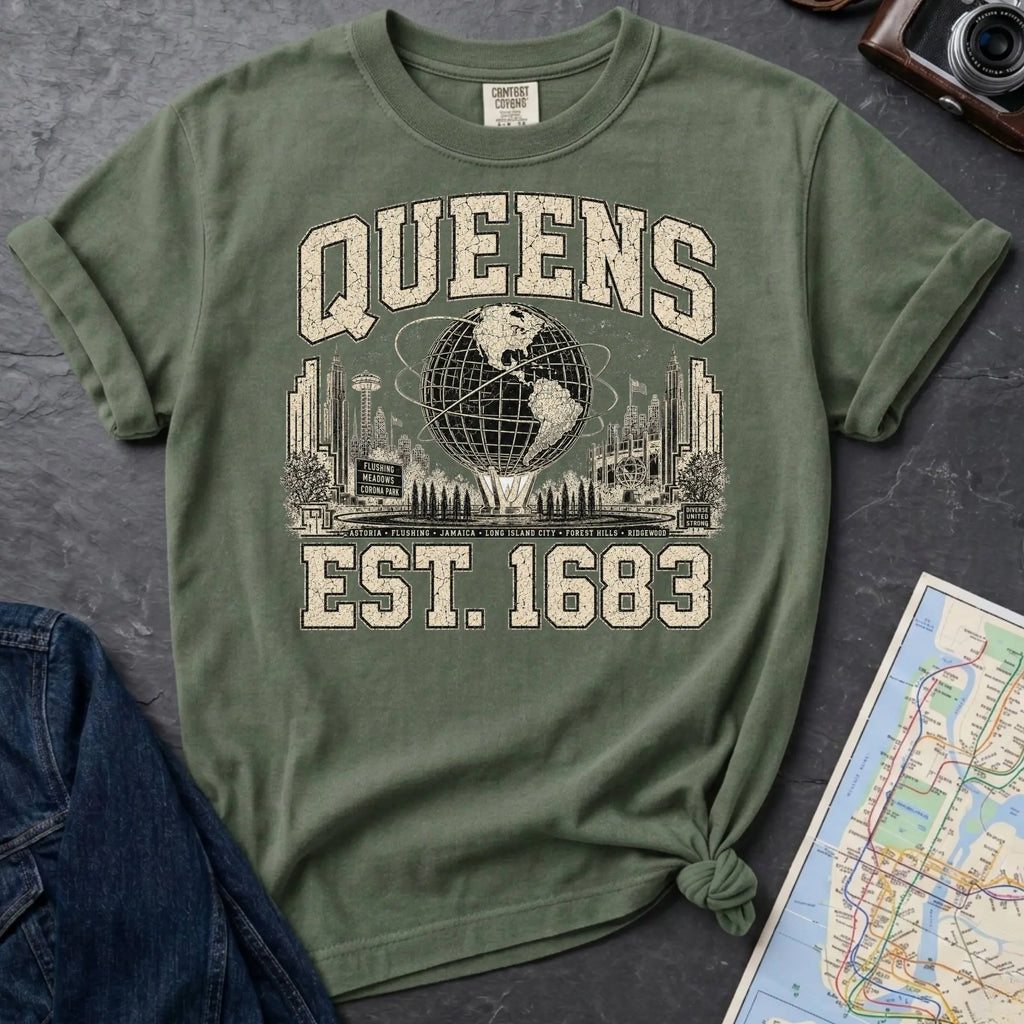Green t-shirt with 'Queens Est. 1683' graphic design on a dark surface with a denim jacket and a map.
