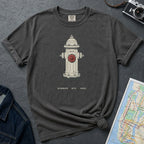 Charcoal colored t-shirt with a fire hydrant graphic and text, placed on a textured surface with a camera and map.