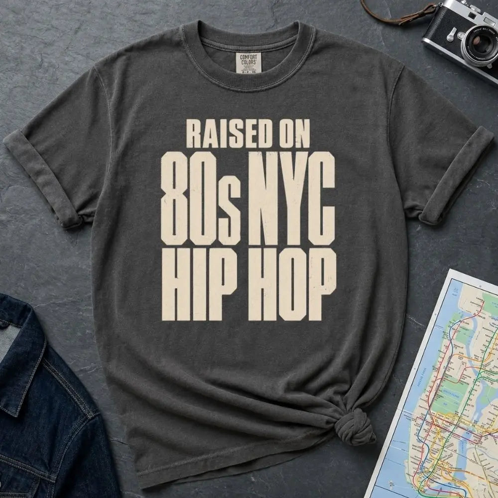 Pepper colored Comfort Colors T-shirt with cream Raised on 80s NYC Hip Hop front print, styled with denim jacket, camera, and subway map