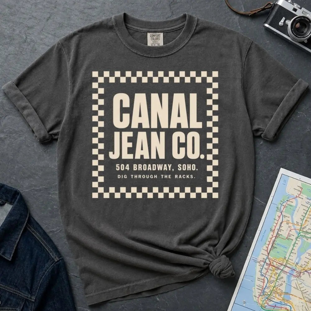 Pepper colored Comfort Colors T-shirt with ivory Canal Jean Co. NYC front print, styled with denim jacket, camera, and subway map.