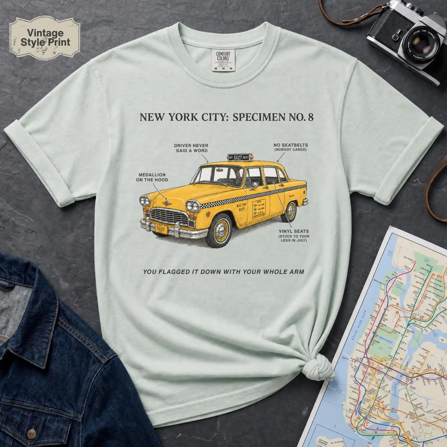 Bay colored Comfort Colors t-shirt with yellow taxi graphic and text on a dark surface with denim jacket and map.
