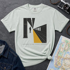 Bay colored t-shirt with a graphic design of a train station platform, denim jacket, and map on a dark surface