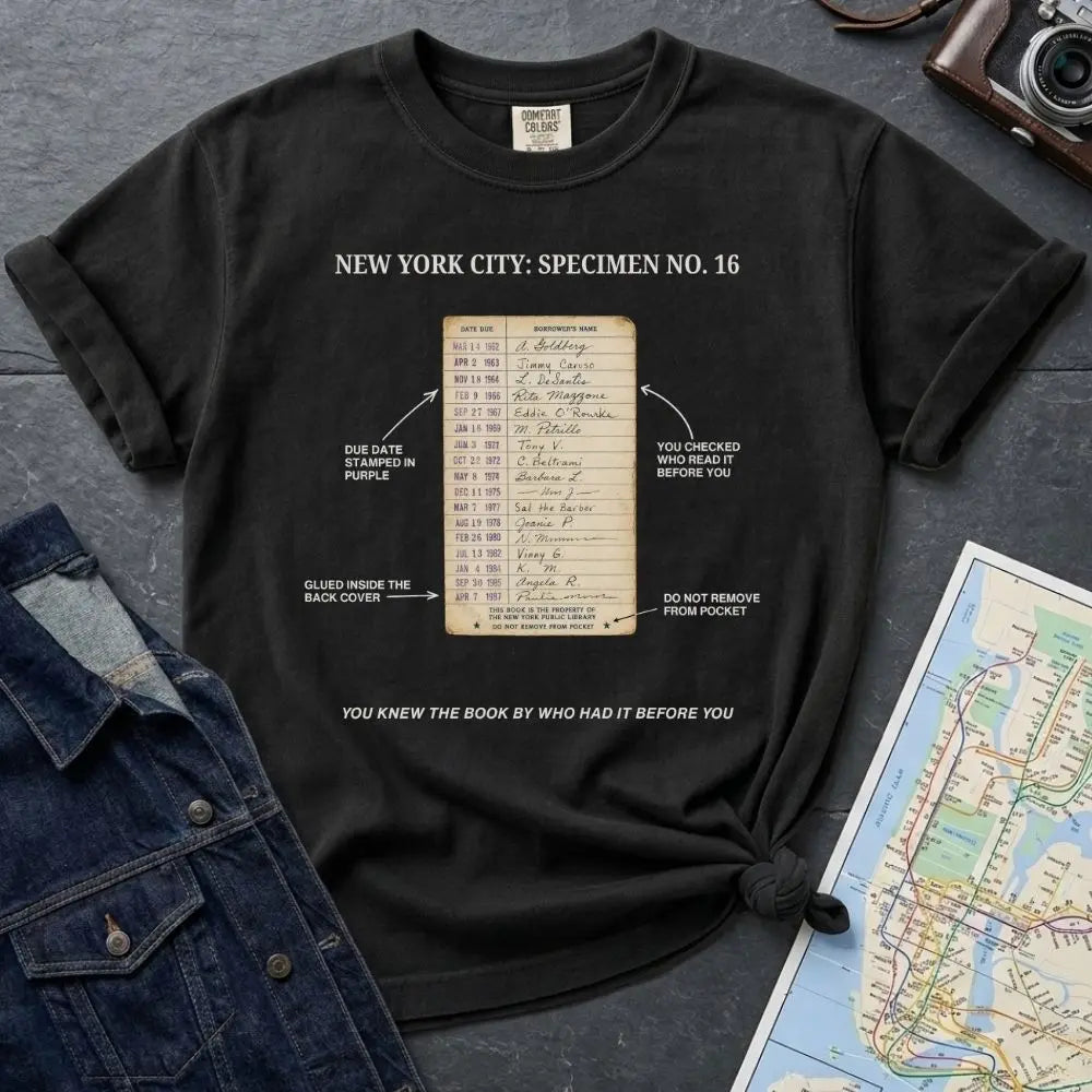 Black Comfort Colors T-shirt with NYC library loan card specimen front print, styled with denim jacket, camera, and subway map